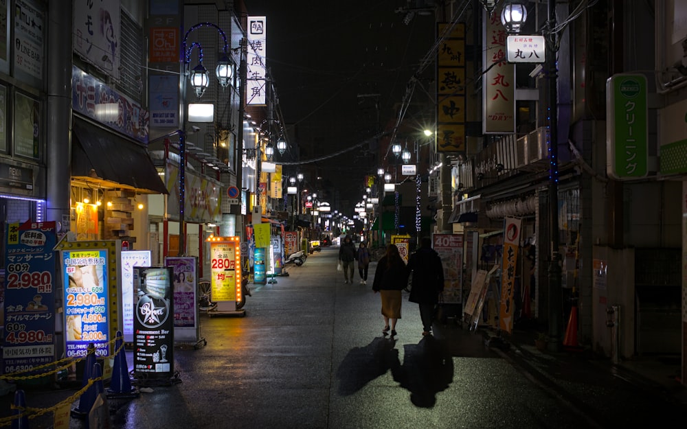 a couple of people walking down a street at night