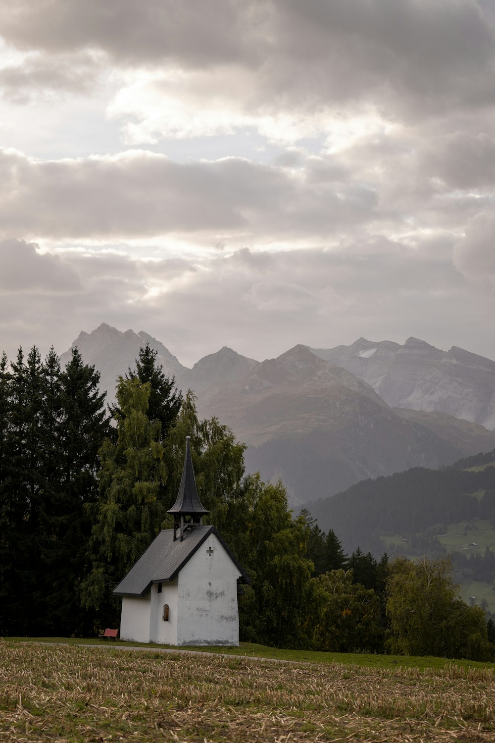 a small church in a field with mountains in the background