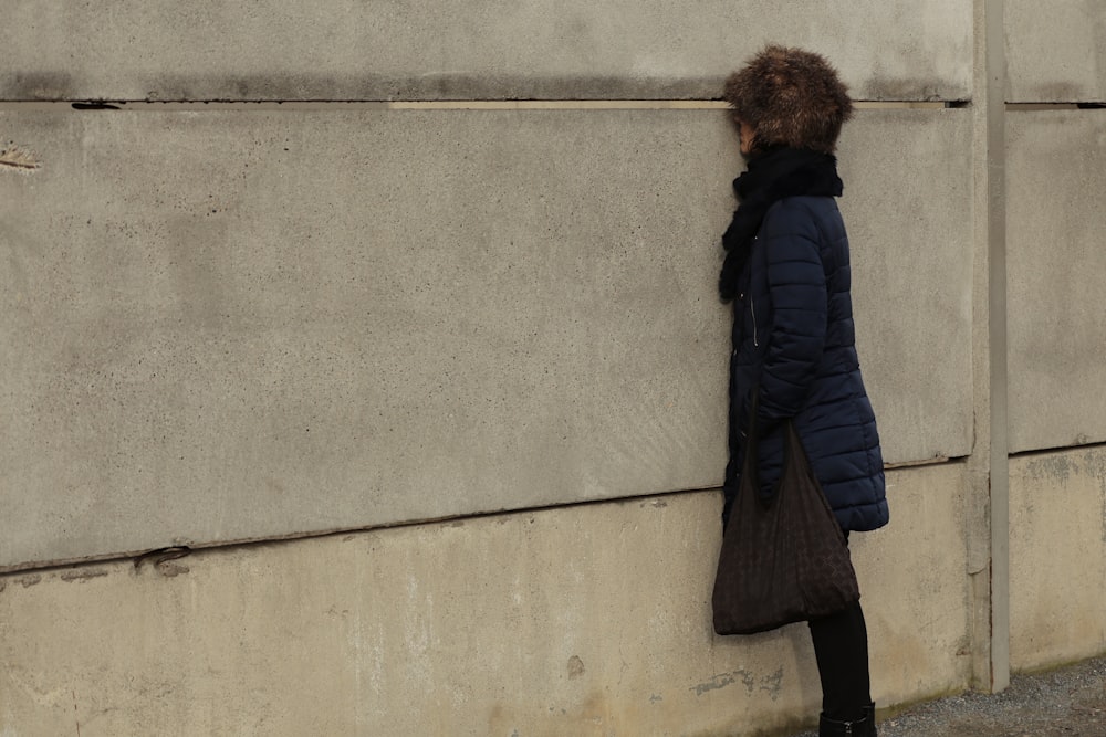 a person leaning against a wall with a coat on