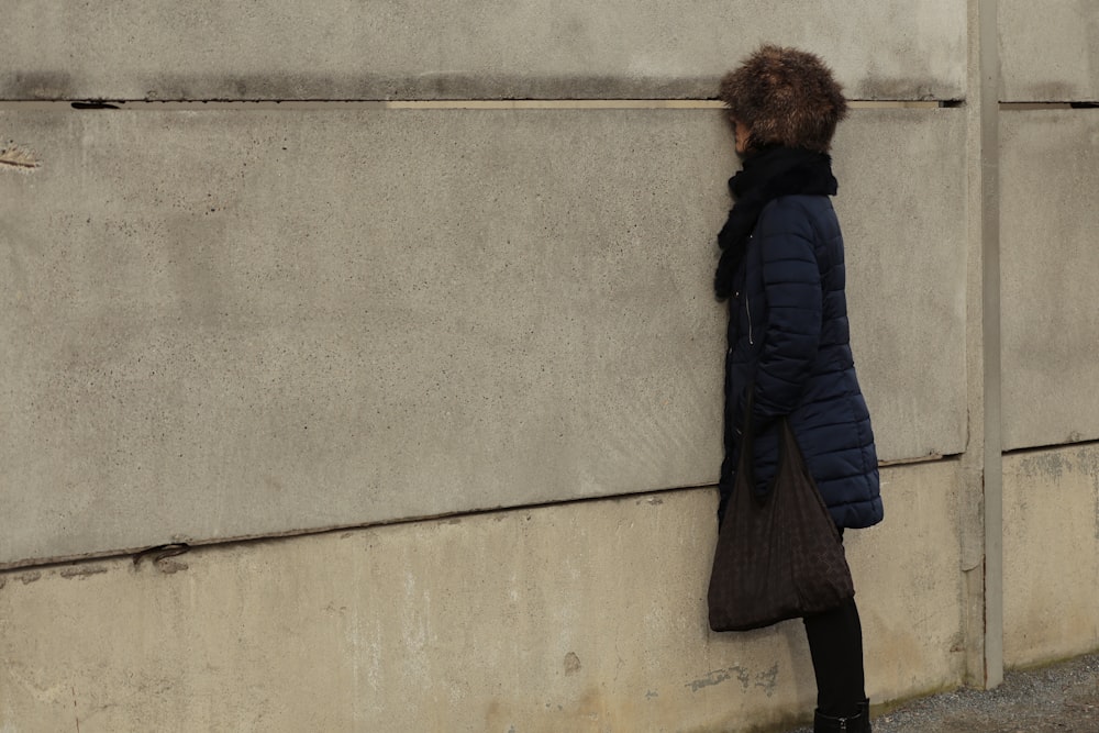 una persona apoyada contra una pared con un abrigo puesto