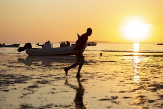 a man running on the beach with a boat in the background