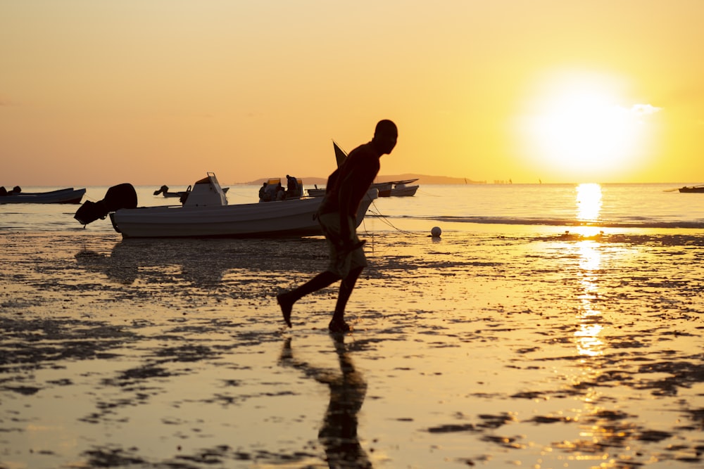 a man running on the beach with a boat in the background