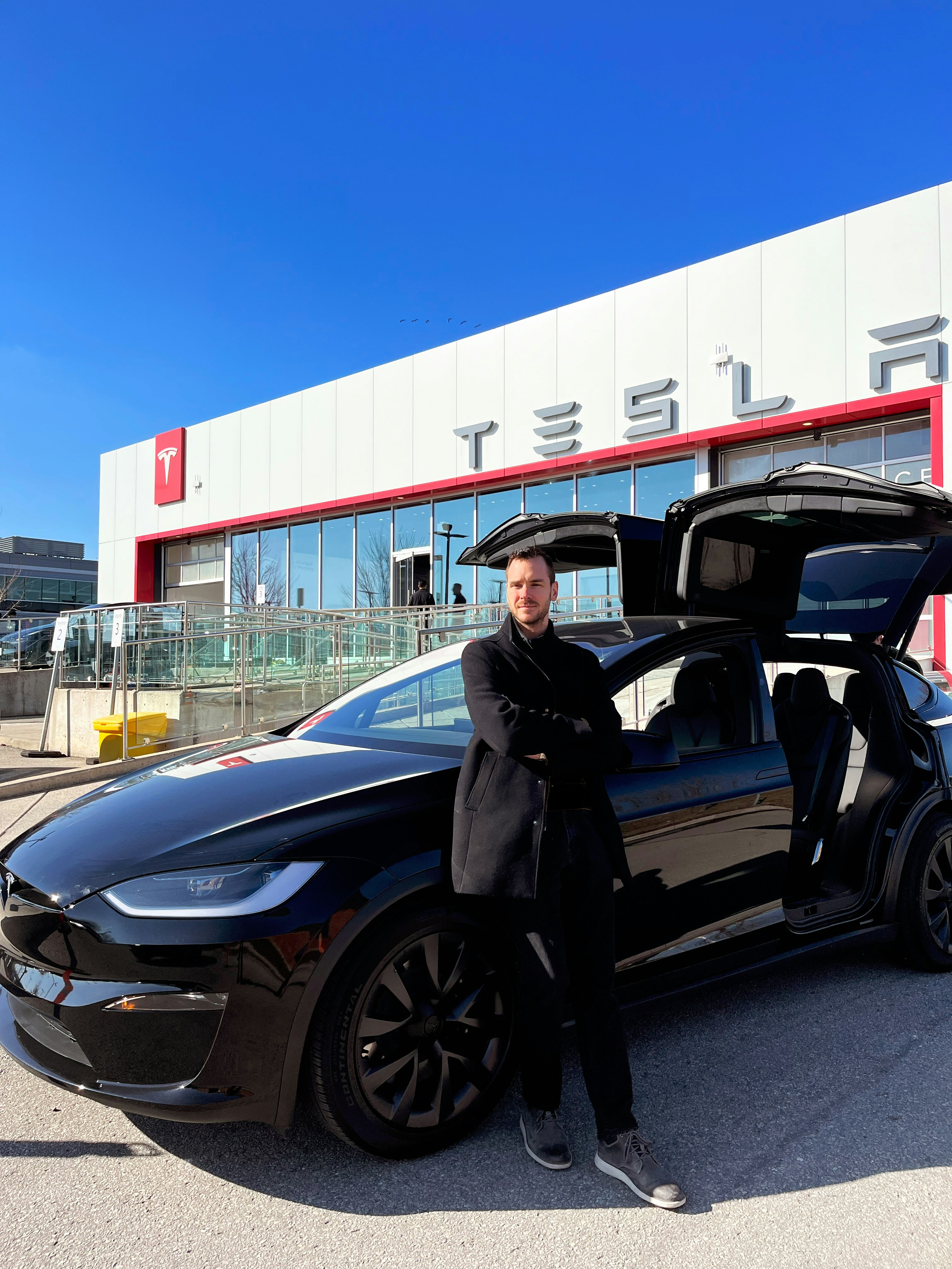 Black Tesla Model X electric SUV in a modern urban environment, sleek exterior with distinctive falcon wing doors open