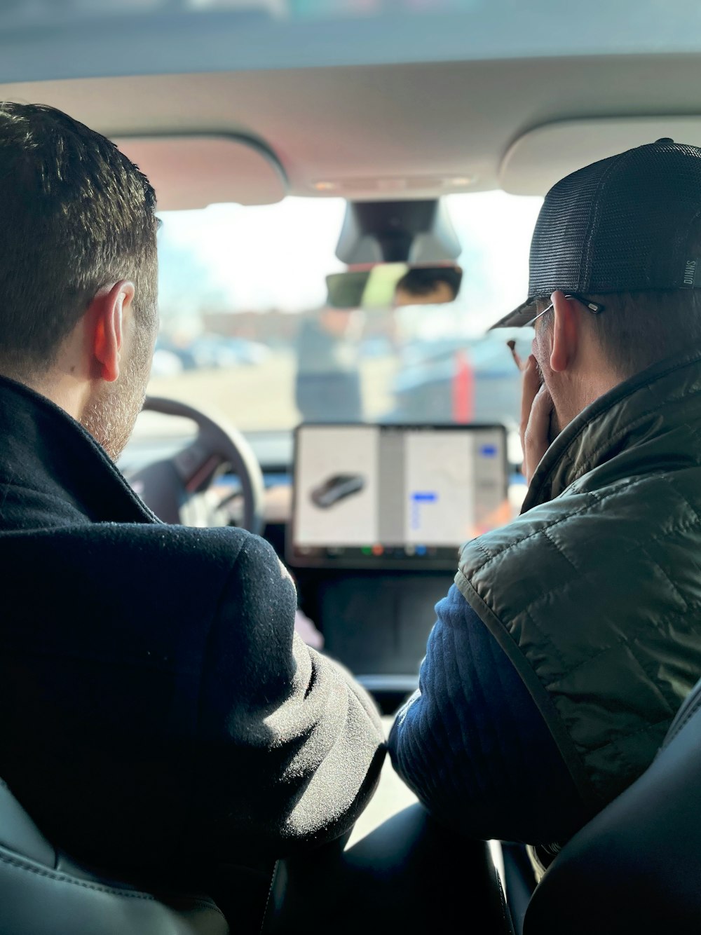 two men sitting in a car talking on their cell phones