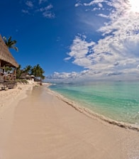 a sandy beach with a thatched roof next to the ocean