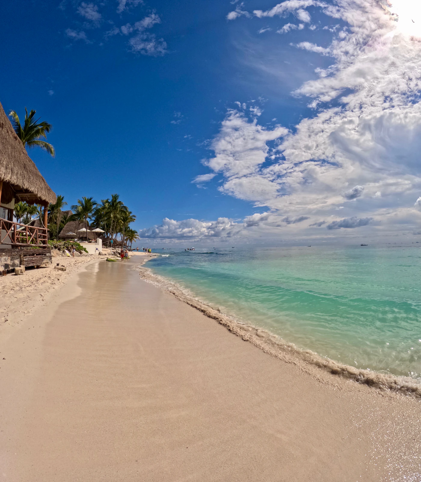 Caribbean beach with a palapa resort building visible on the shoreline, white sand stretching along the coast with turquoise sea and a wide sky above