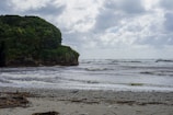a beach with a rock outcropping in the middle of the ocean