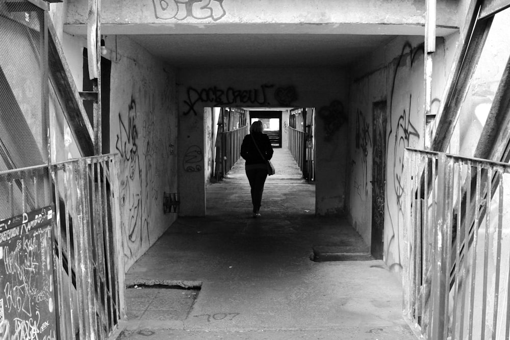 a black and white photo of a person walking down a tunnel