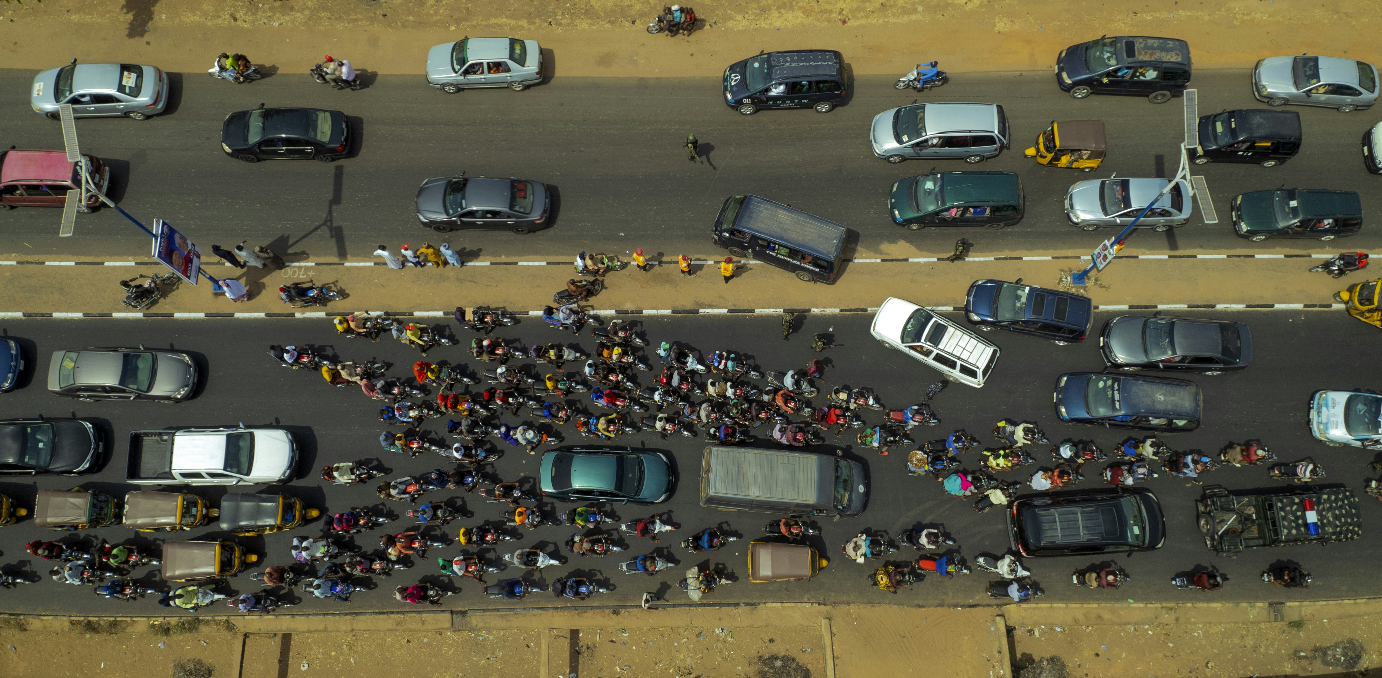 A large political rally with many cars lined up on a road, people gathered around, a banner of 'Kisan Morcha' visible in Hindi, depicting an energetic but crowded scene.
