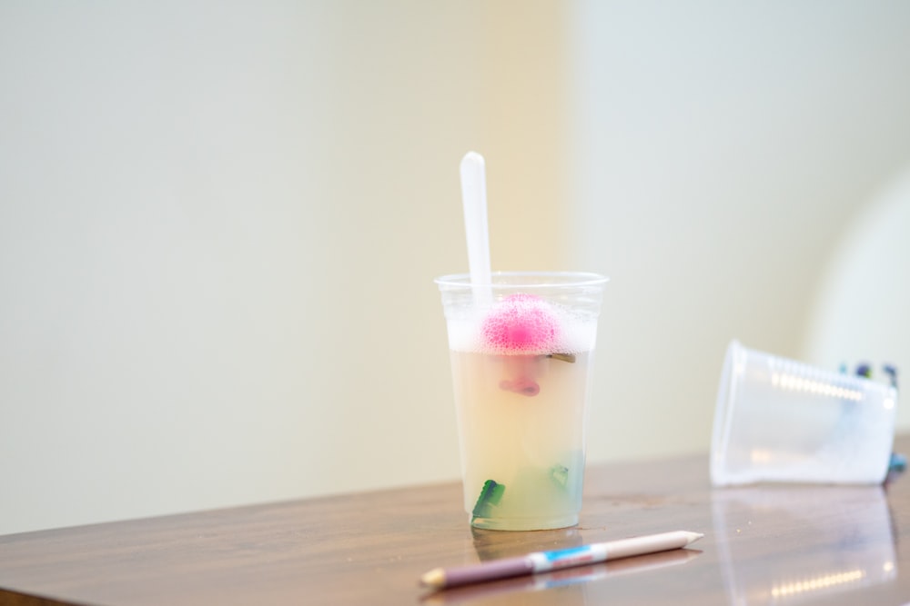a plastic cup with a straw and a pink ball in it