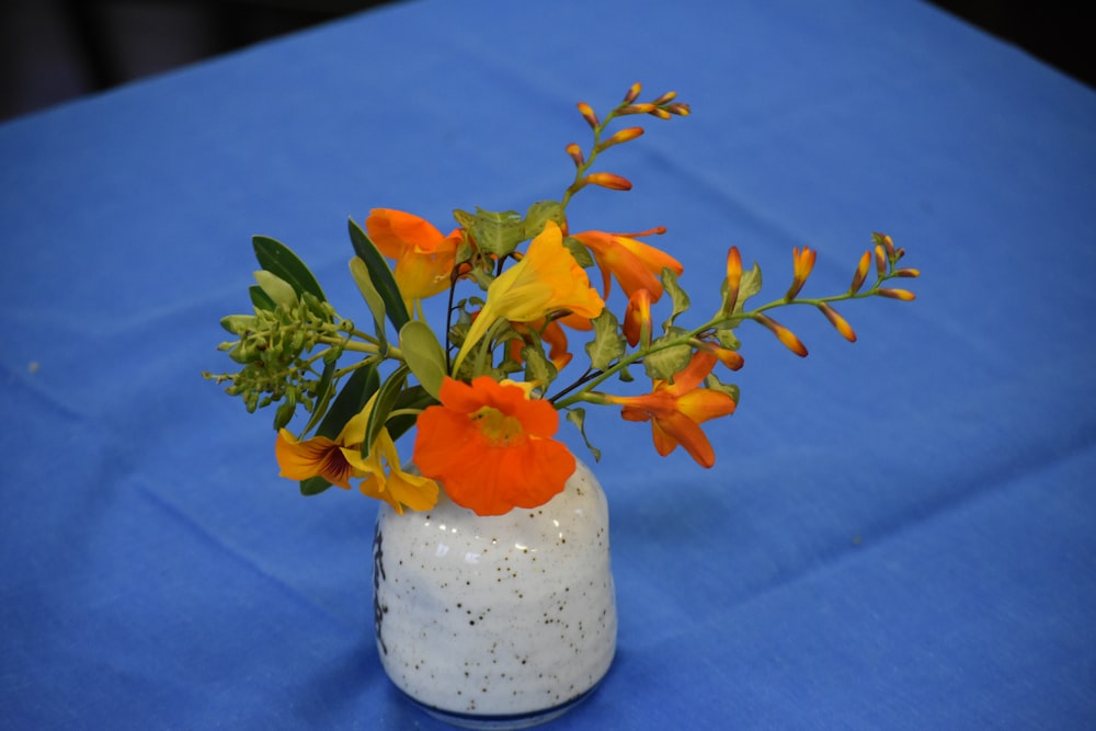 un vase blanc rempli de fleurs oranges et jaunes