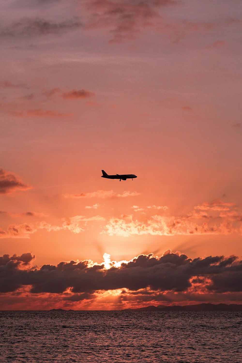 a plane flying over the ocean at sunset
