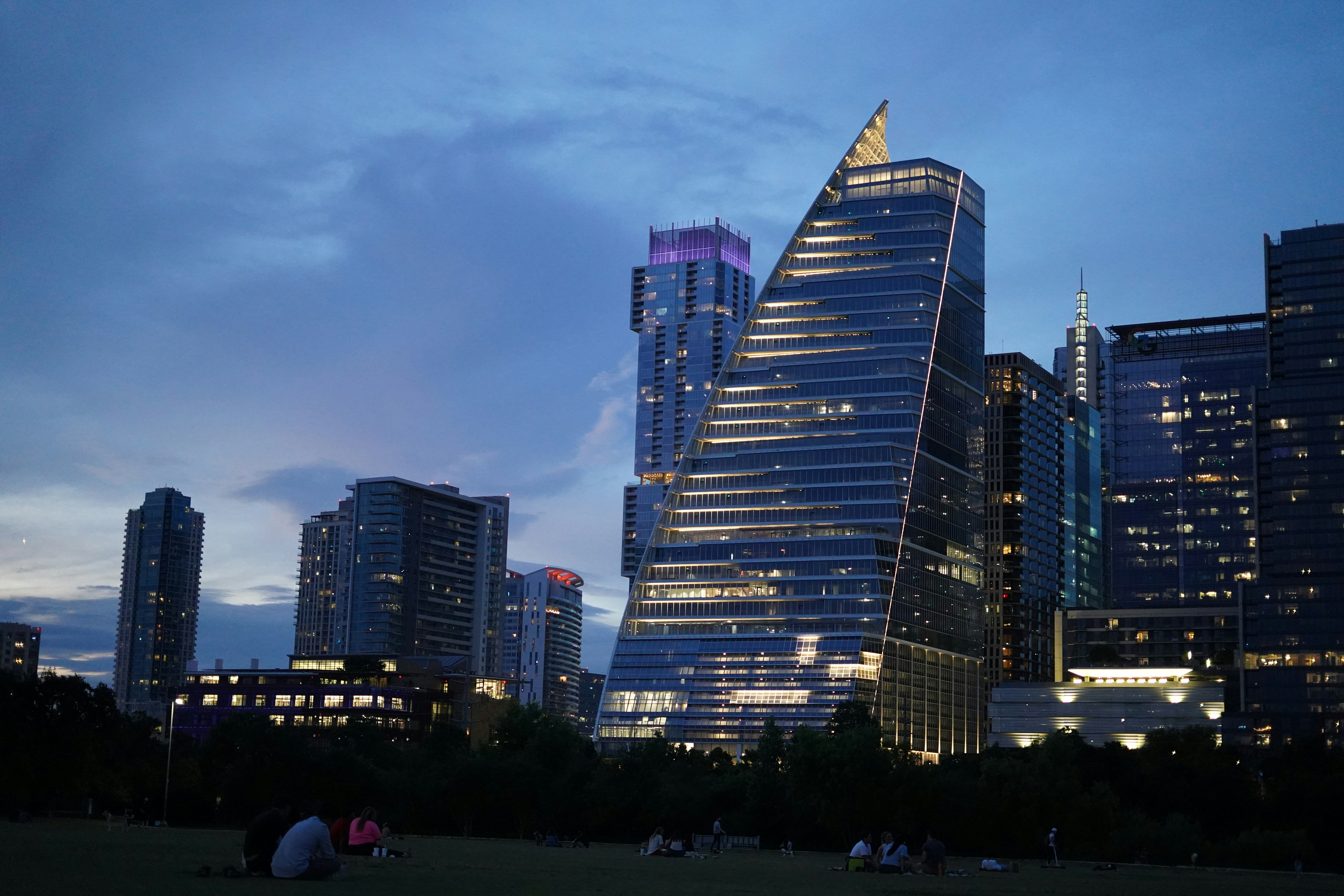 un gruppo di persone sedute nell'erba di fronte a edifici alti