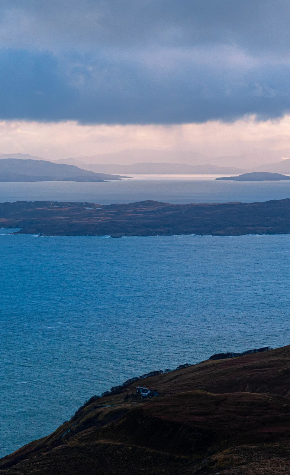 The image depicts a serene coastal scene with a deep blue ocean stretching out to meet a light brown cliff on the right side, creating a striking contrast between the two colors. The sky above is filled with clouds, adding depth and texture to the landscape. In the distance, several islands can be seen, their white and gray hues blending harmoniously with the overcast sky. A small boat is visible in the water near the cliff's edge, suggesting that this picturesque location might be a popular spot for sailing or boating activities.

The image does not contain any discernible text or countable objects, making it an open-ended visual experience focused on capturing the beauty of nature and the vastness of the ocean.