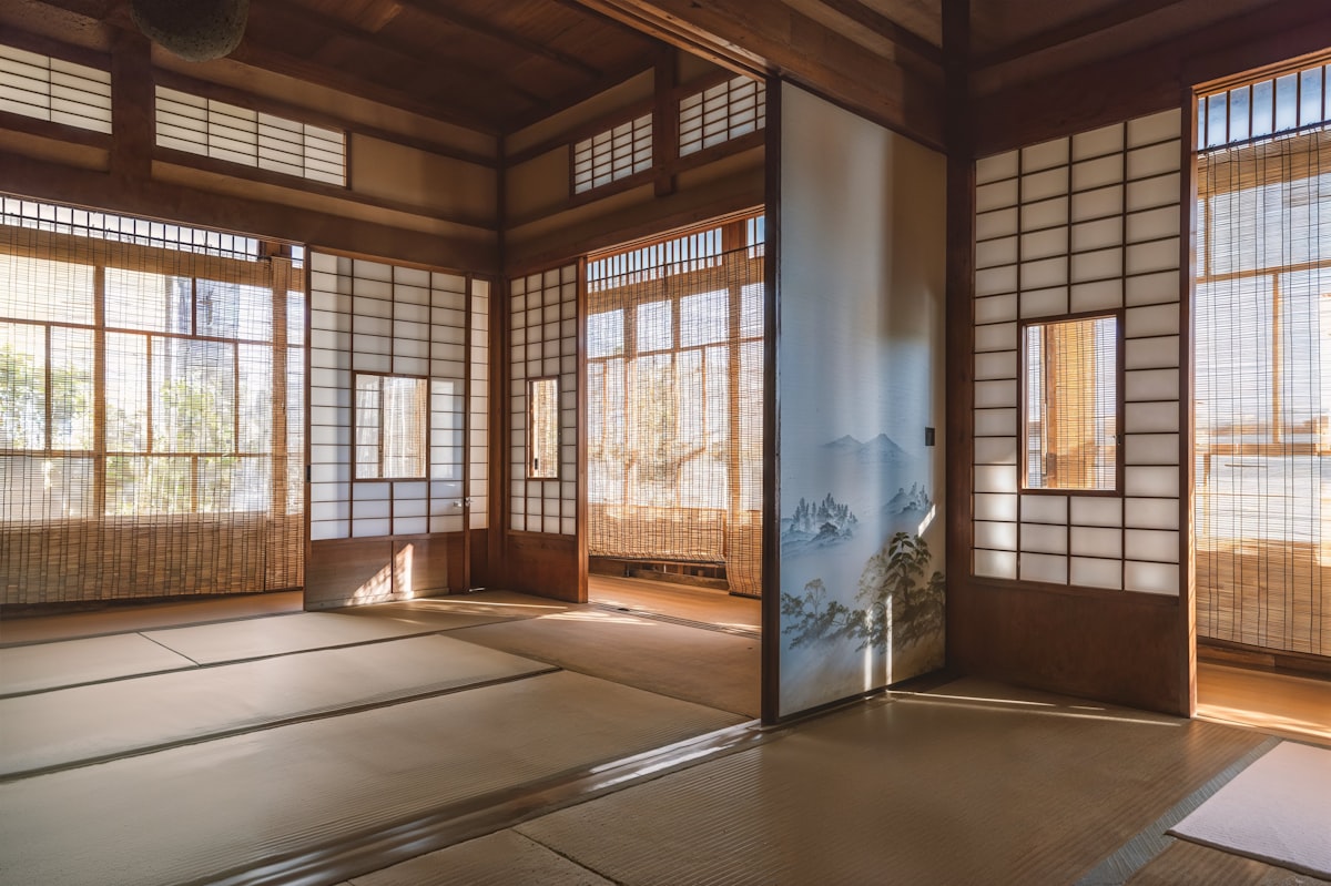 A sunlit traditional Japanese room with tatami floors, shoji screens, and warm wooden beams
