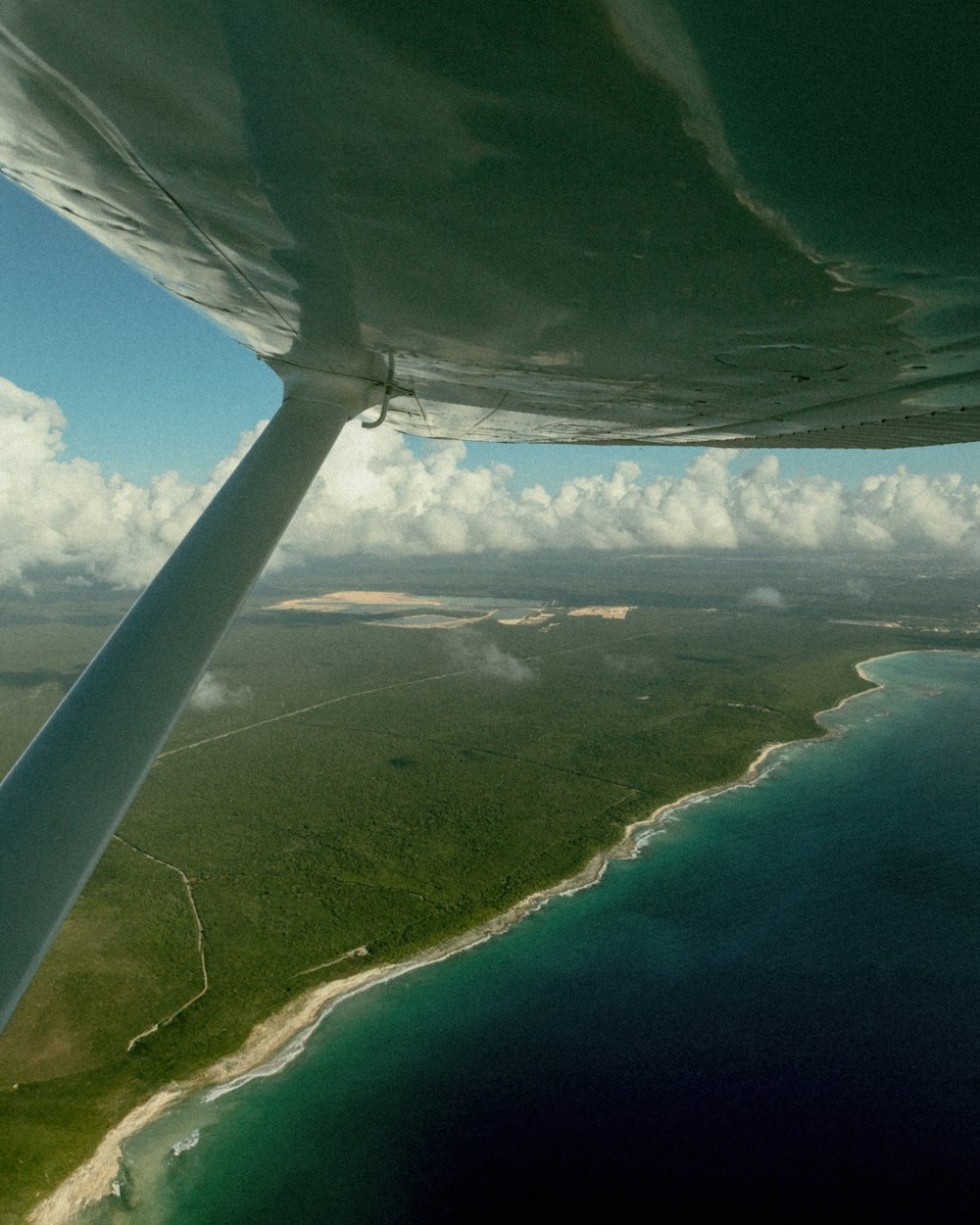 the wing of a plane flying over a beach