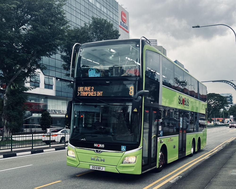 a green double decker bus driving down a street