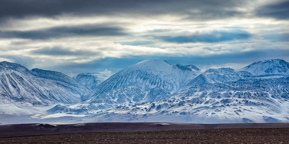 a mountain range covered in snow under a cloudy sky