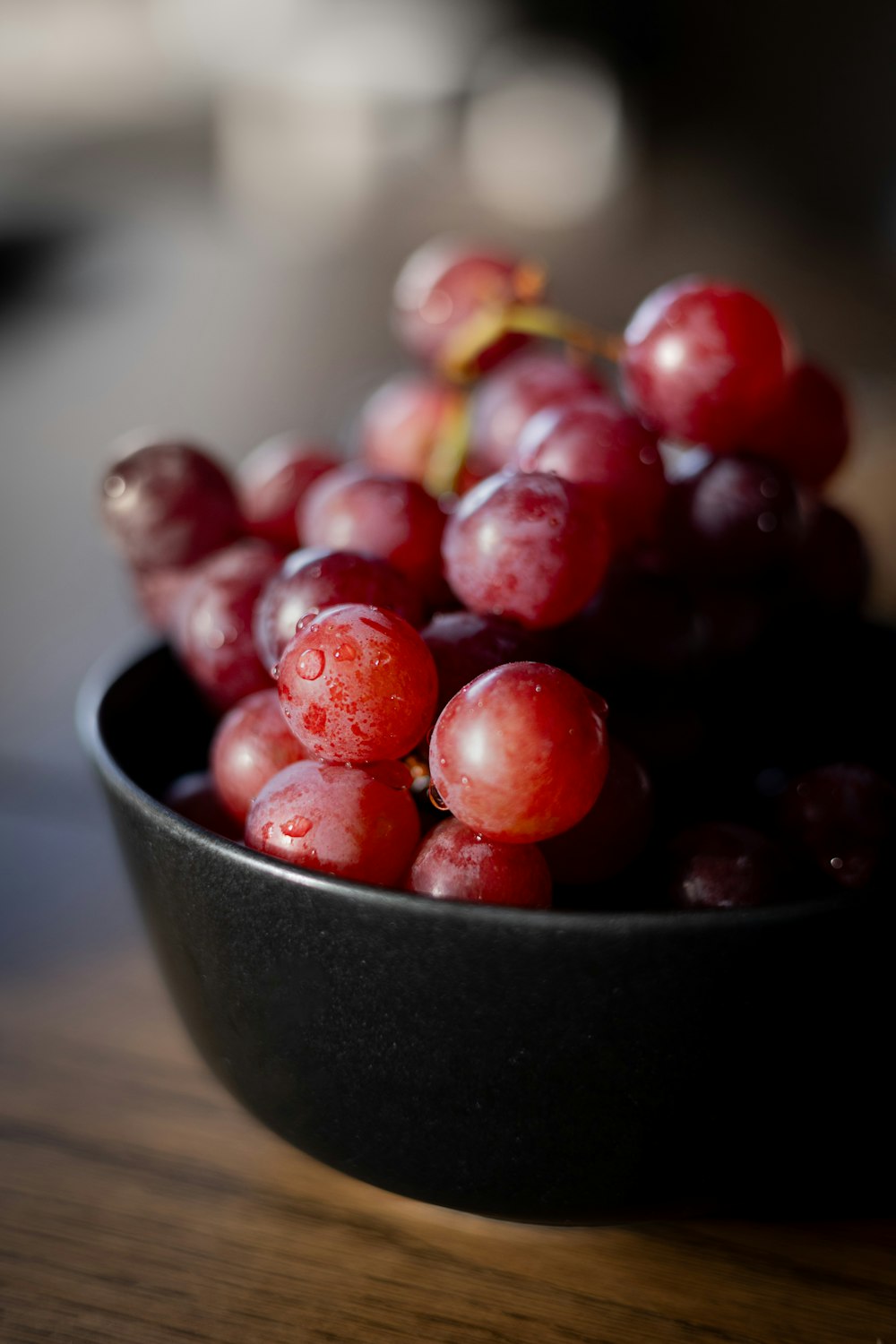a black bowl filled with red grapes on top of a wooden table