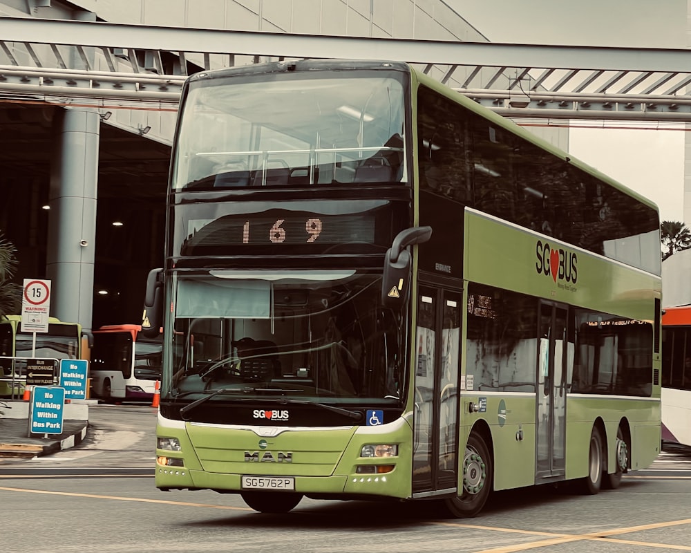 a green double decker bus driving down a street