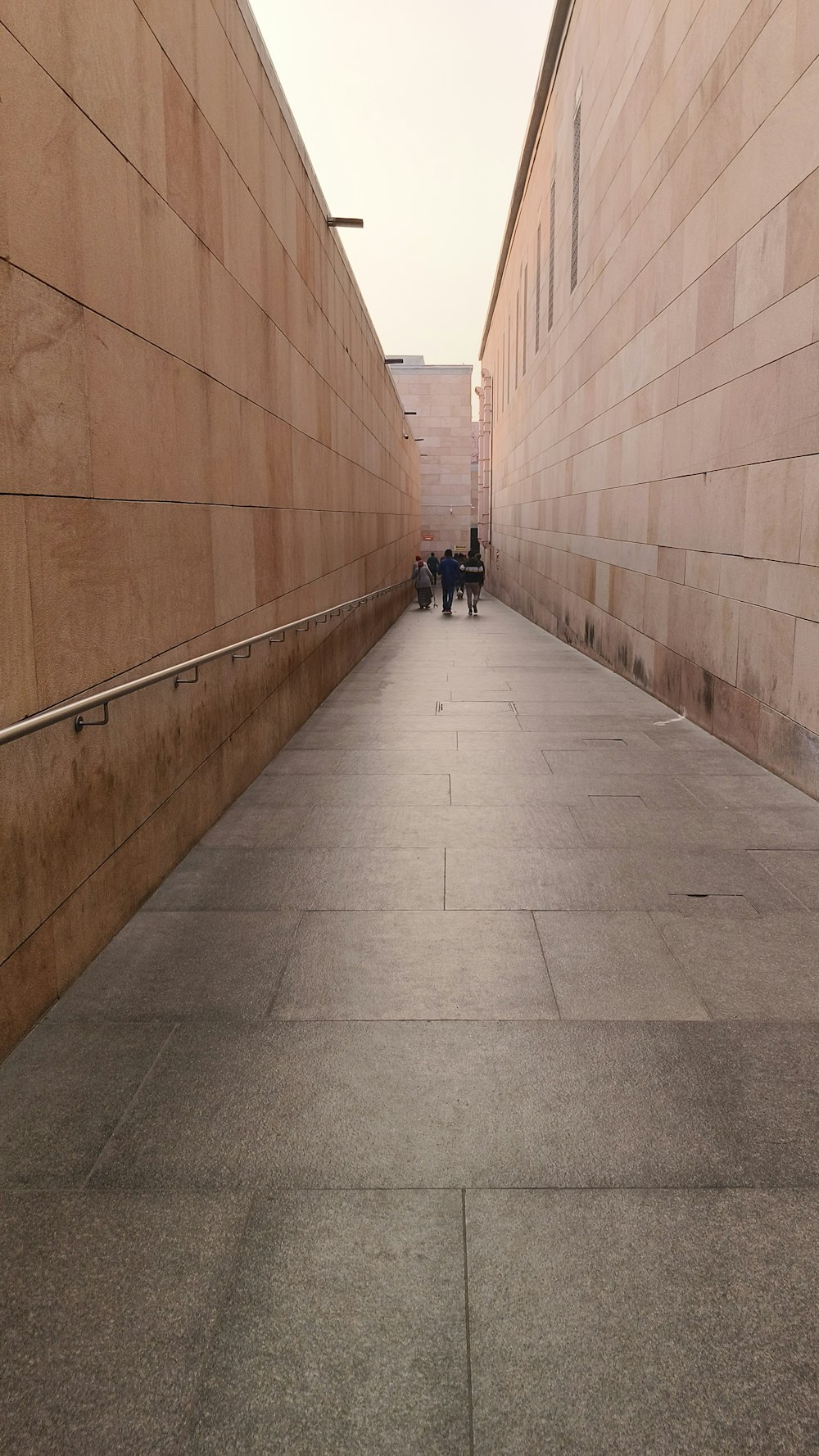 a couple of people walking down a sidewalk next to a wall