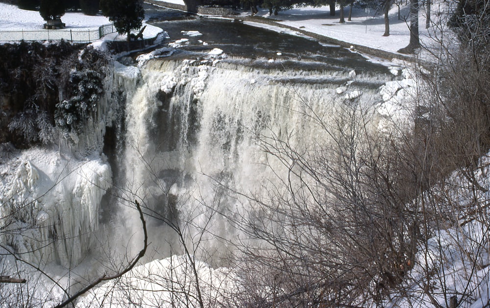 a large waterfall with snow on the ground