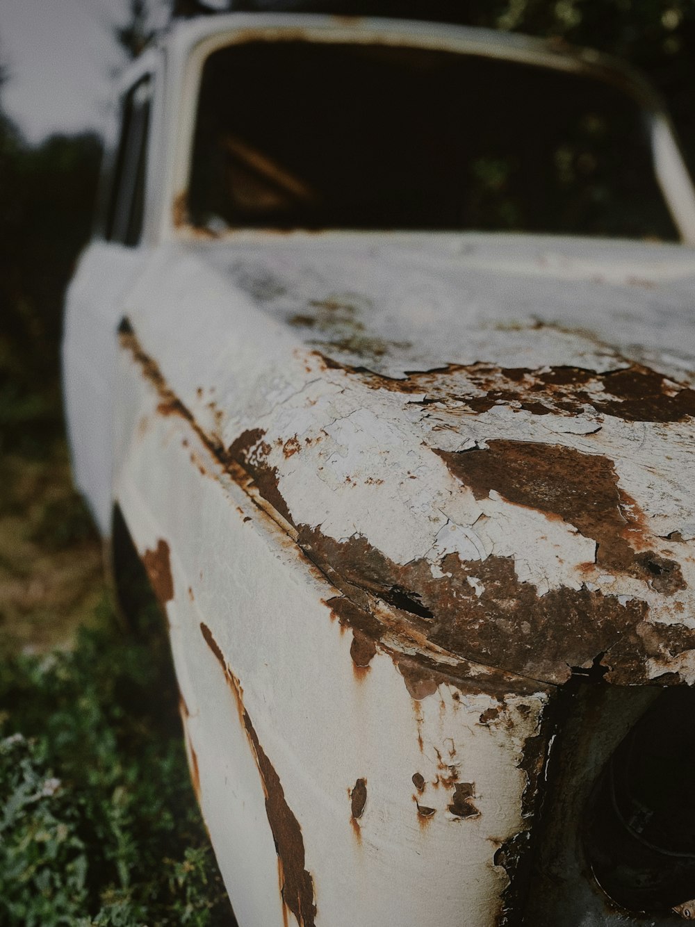 an old rusted out car sitting in the grass