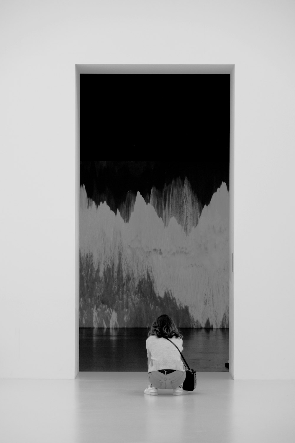 a black and white photo of a person sitting in front of a painting