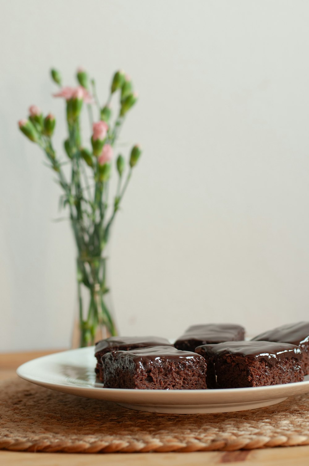 a white plate topped with chocolate cakes next to a vase of flowers