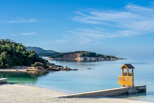 A wooden bench sitting on top of a sandy beach — Ksamil, Albania