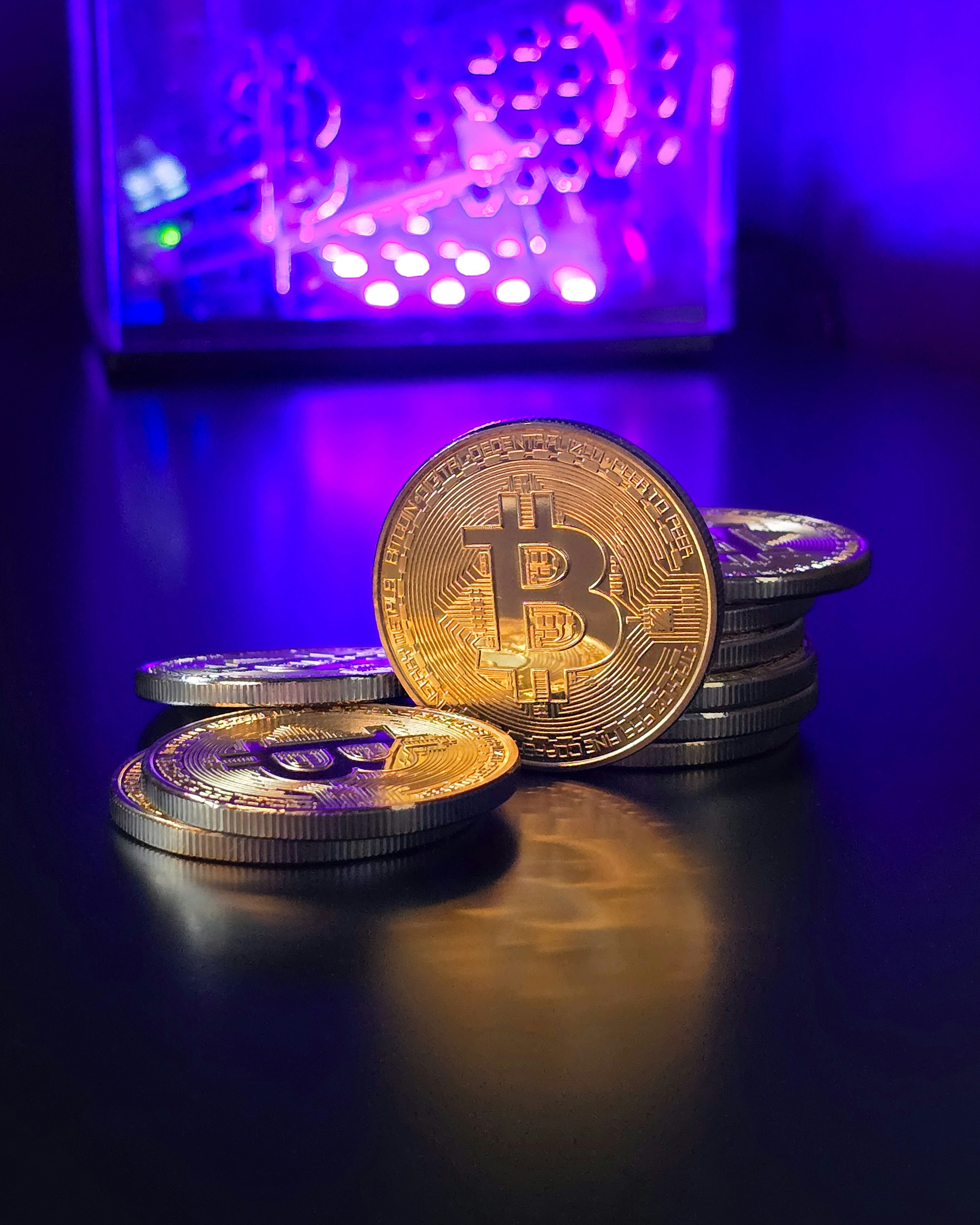 Shiny gold Bitcoins against blue and purple background. The future of money, reinvented. Portrait mode.