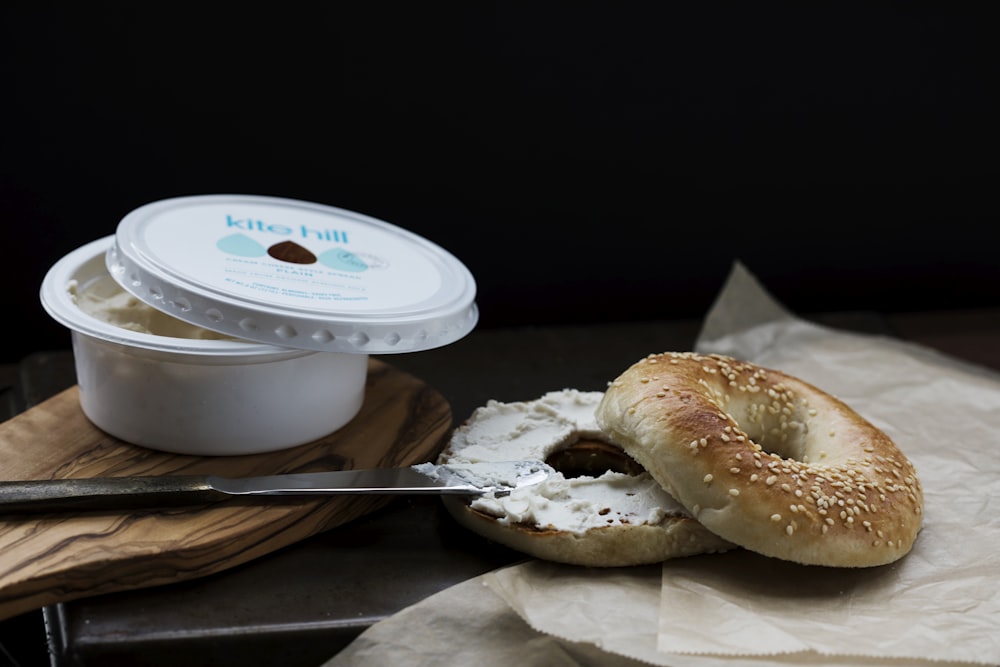 a bagel sitting on top of a wooden cutting board next to a container of