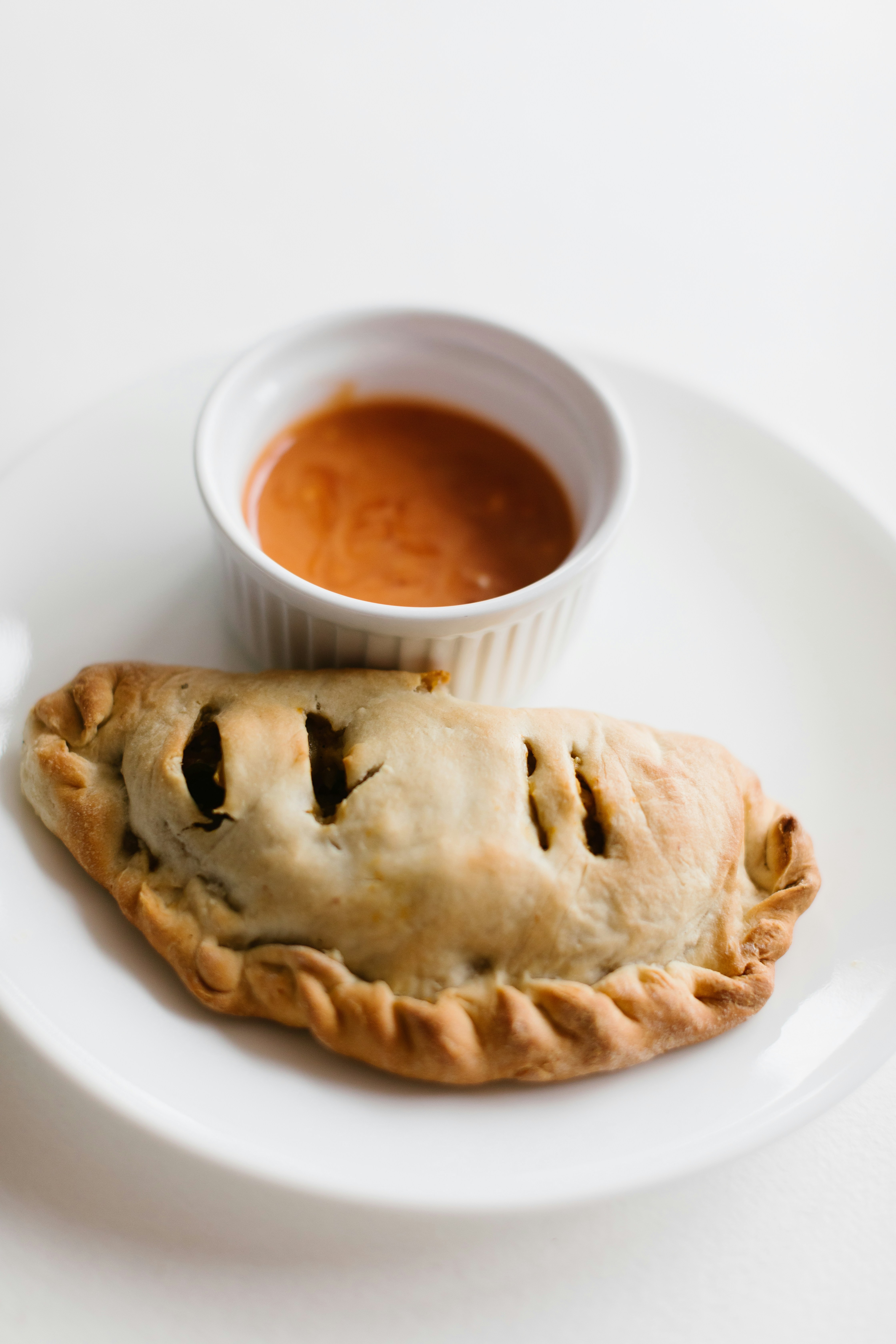 a white plate topped with a pastry next to a bowl of sauce