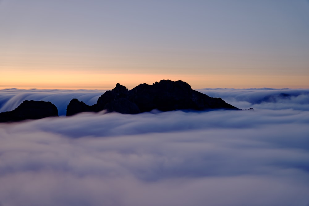 a mountain covered in clouds with a sunset in the background