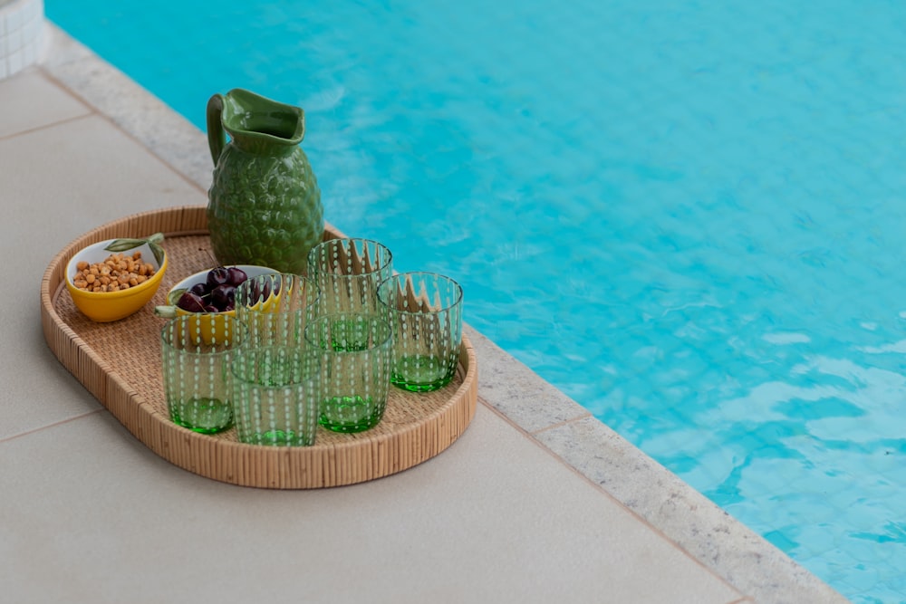 a bowl of fruit and a pitcher of water on a tray next to a pool