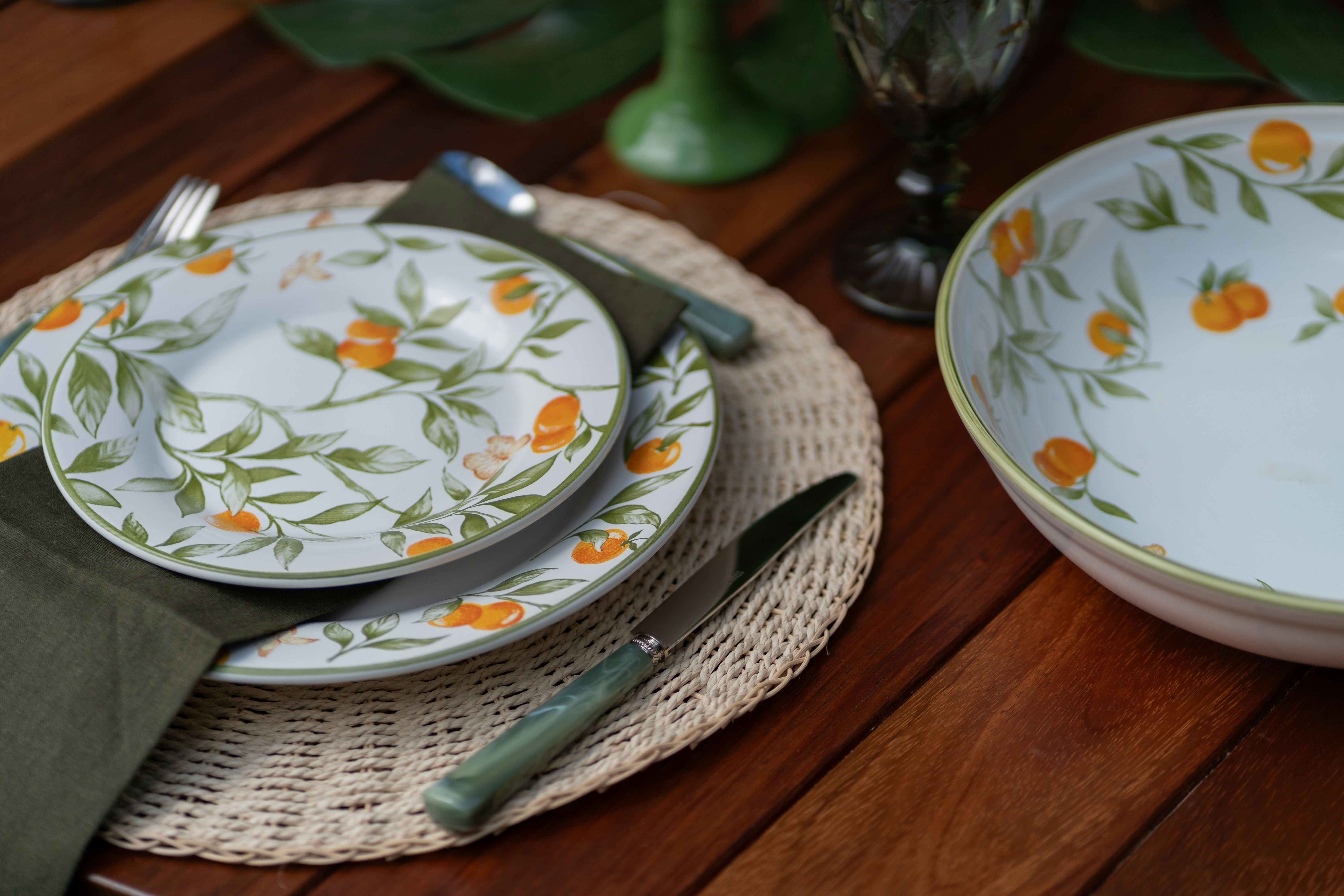 a place setting with a green napkin and a white plate with orange flowers
