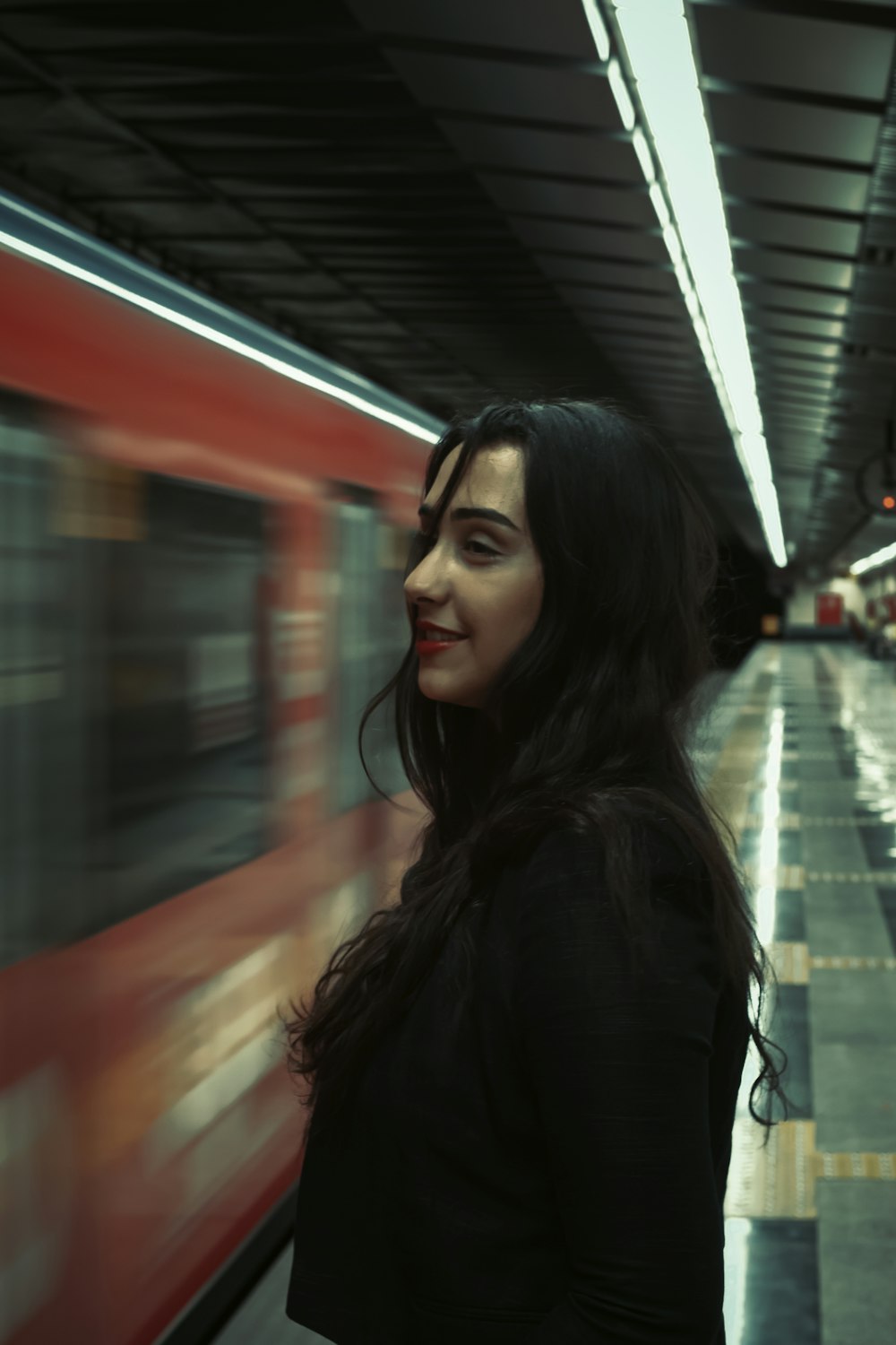 a woman standing in a subway station waiting for a train
