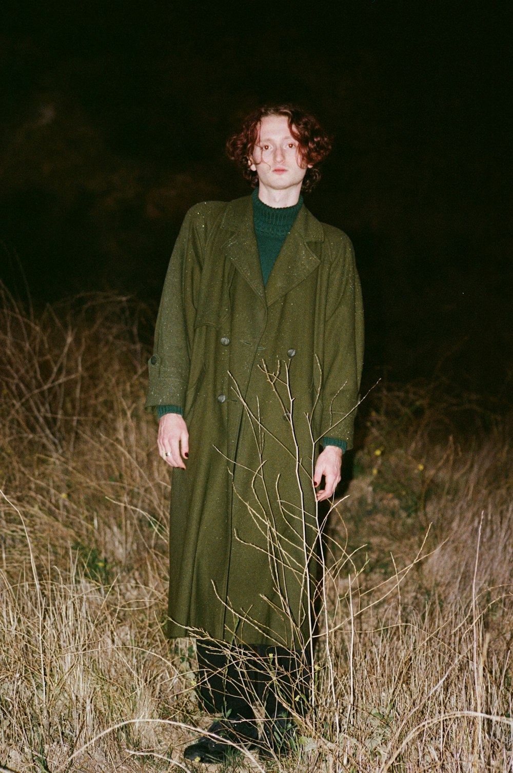 a woman in a green coat standing in a field