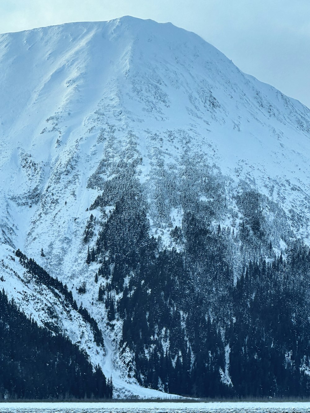 uma montanha coberta de neve ao lado de um corpo de água