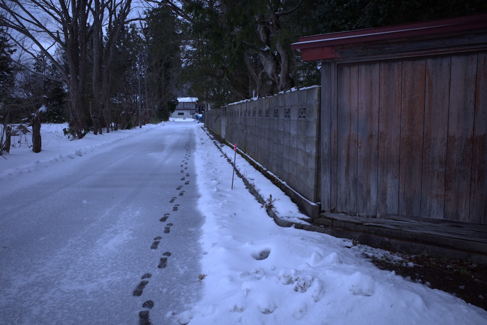 a snow covered street with a fence and trees