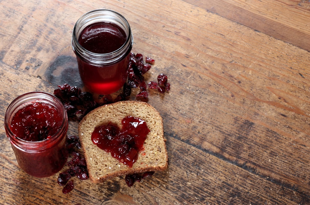 two jars of jam sit next to a piece of bread