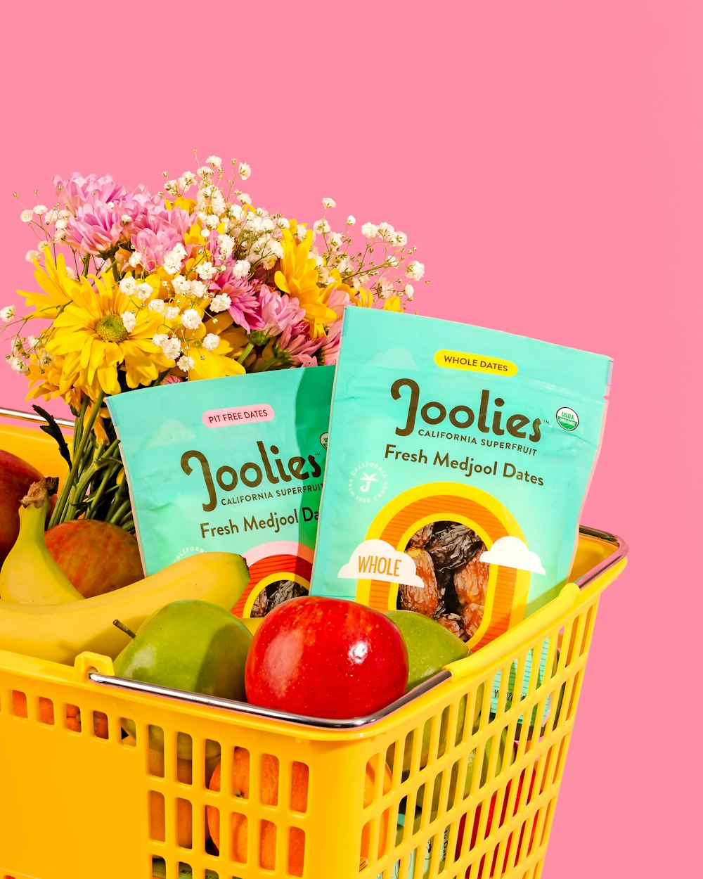 a basket filled with fruit and snacks on a pink background