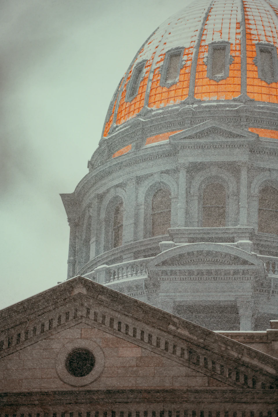 The image shows a majestic, large dome-shaped building with a blend of white and gray colors. The building features multiple windows that add to its architectural charm. The perspective is from below, looking up at the structure, emphasizing its grandeur. The sky above is overcast, casting a soft light on the scene.