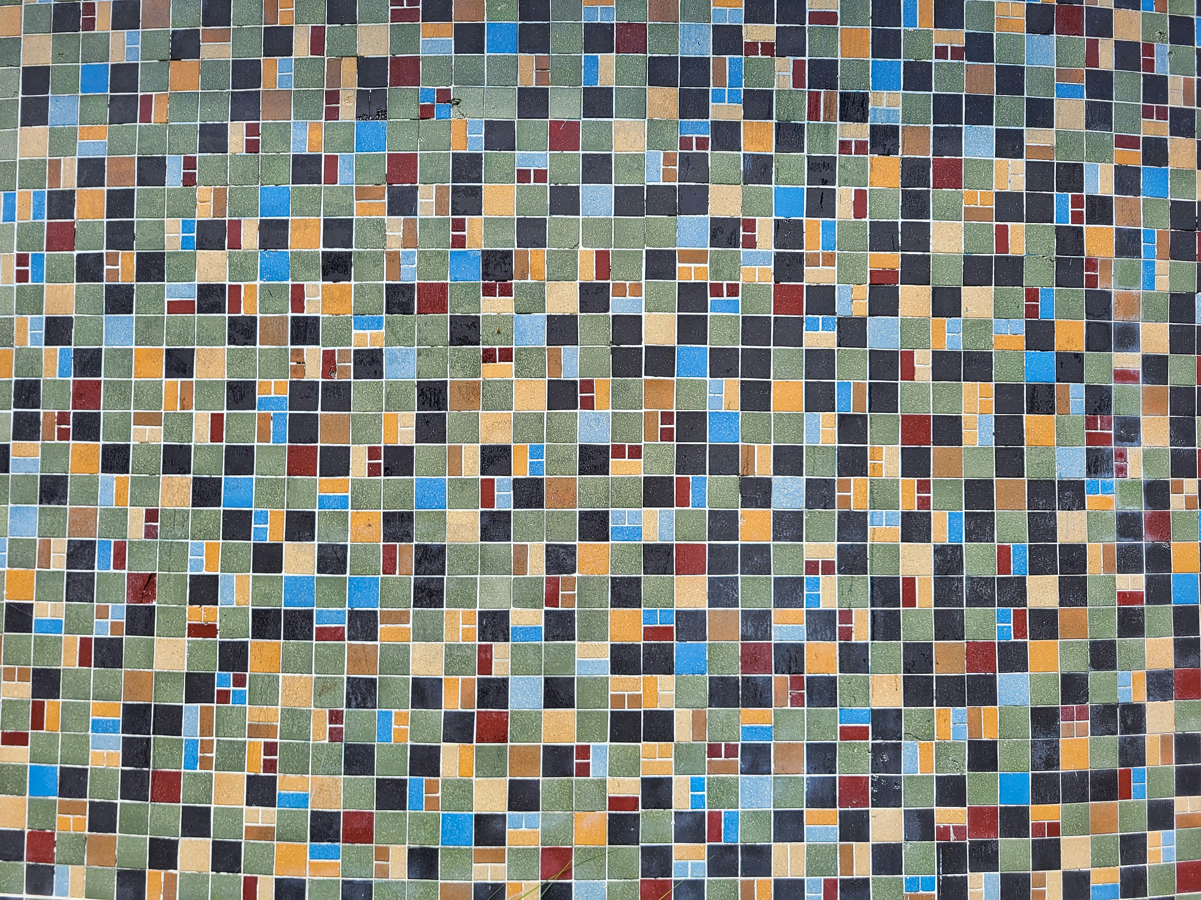 a multicolored tiled wall with a black cat sitting on top of it