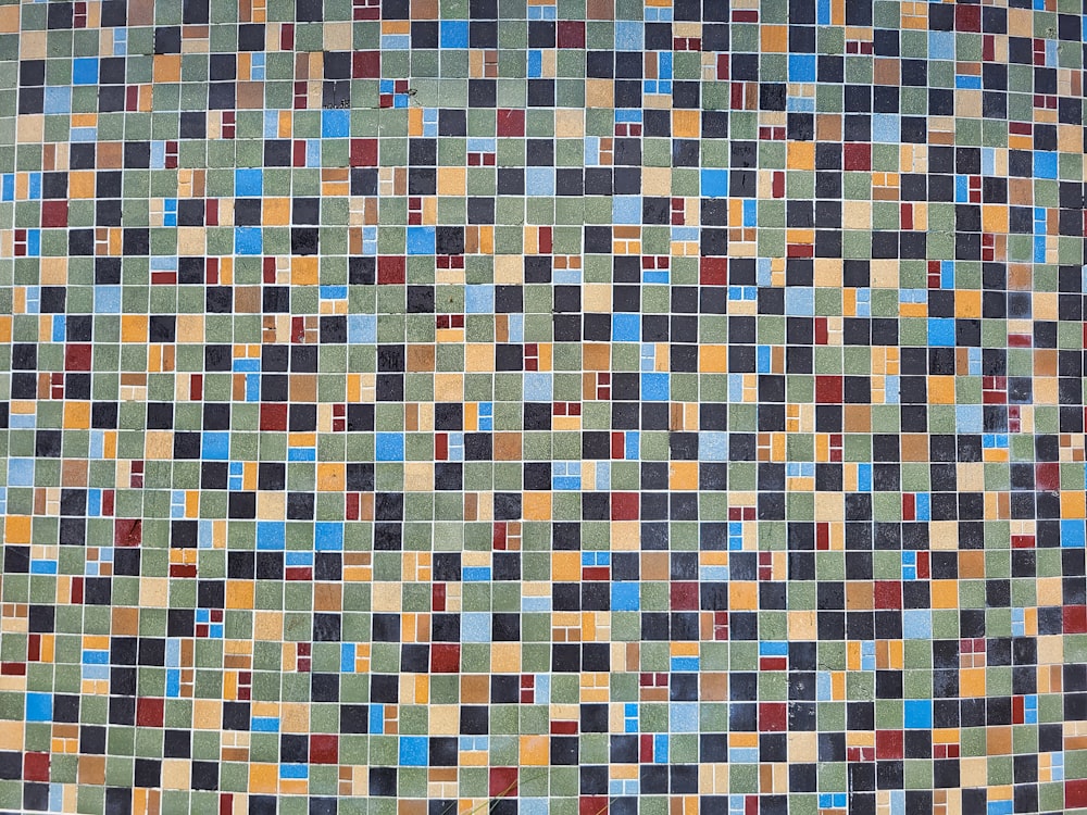a multicolored tiled wall with a black cat sitting on top of it