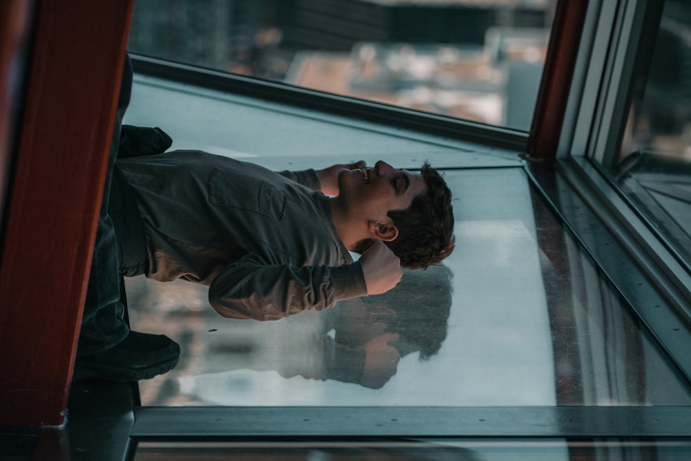 a young man leaning against a window looking up