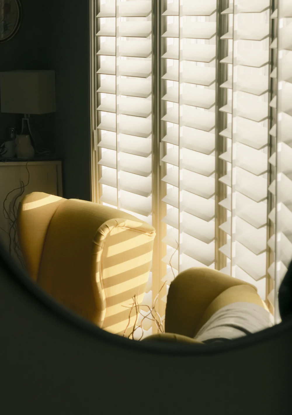 A bright living room with white plantation shutters and a cream armchair
