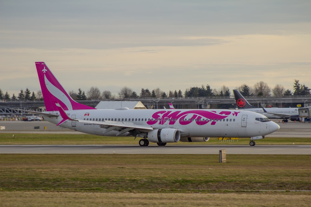 a pink and white plane is on the runway