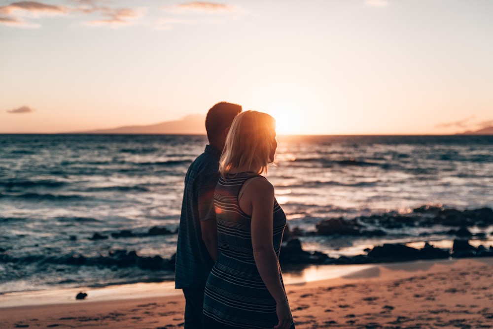 un homme et une femme debout sur une plage au coucher du soleil