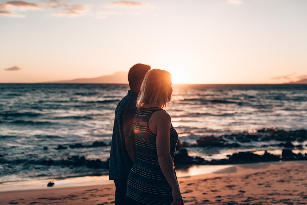 a man and a woman standing on a beach at sunset